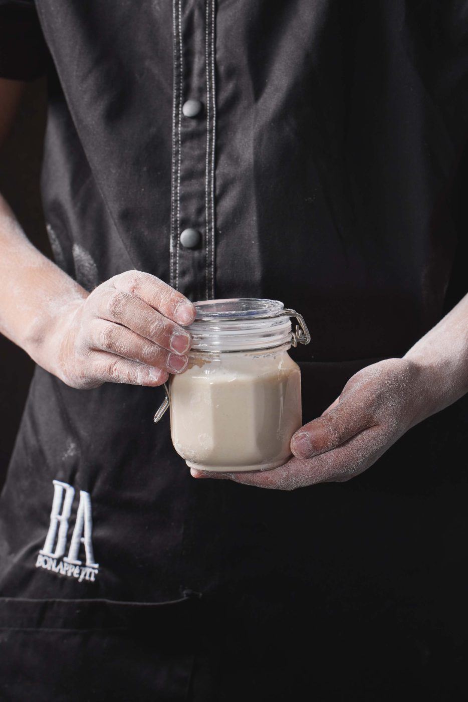 A BA baker holding a jar of sourdough starter
